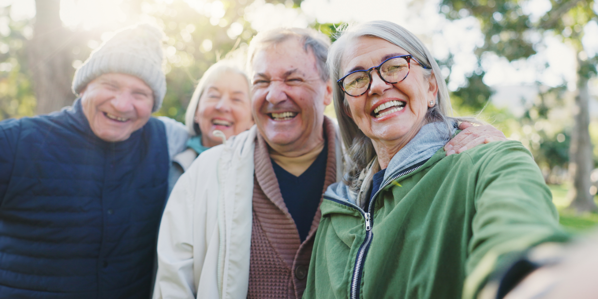 Four older friends laughing together and taking a selfie outdoors